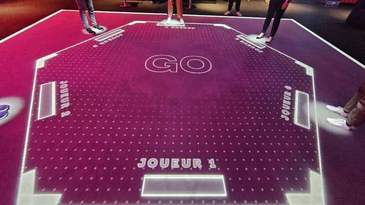 Six people stand around a projected game board on the floor with the word 